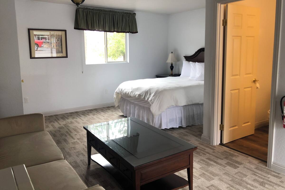 A bedroom with a bed, a nightstand, a lamp, a window, a ceiling fan, and a door.