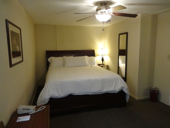 A hotel room with a bed, a ceiling fan, a bedside lamp, a telephone, and a trash bin. - Bay Meadows Resort (Big Bear Lake)