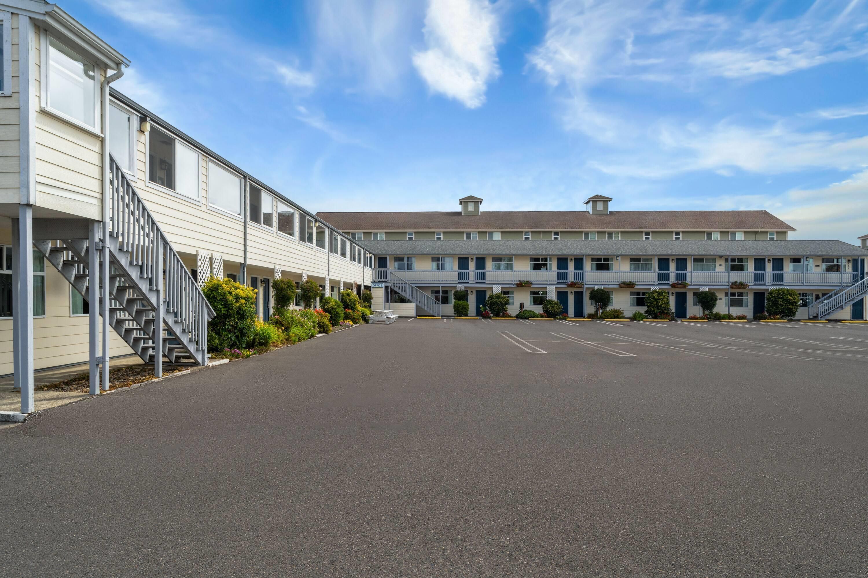 A hotel with a parking lot, a staircase on the left, and a row of rooms with balconies.