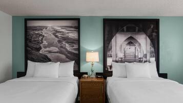 Een hotelkamer met twee bedden, een nachtkastje met een lamp, en twee grote, ingelijste foto’s aan de muur.