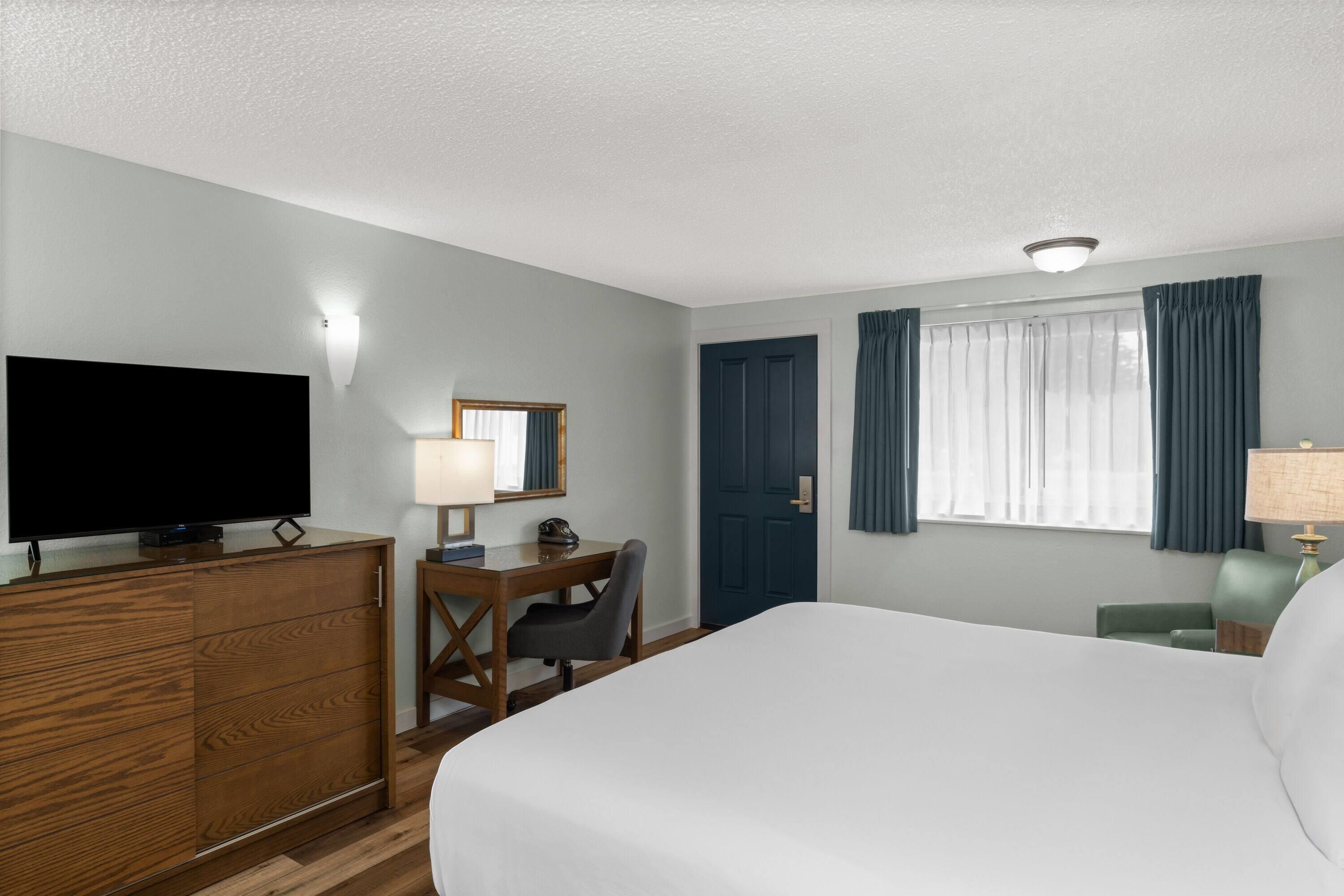 A hotel room with a bed, a desk, a television, a chair, and a window with curtains.