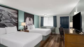 A hotel room with two beds, a desk, a chair, a television, and a large window with curtains.