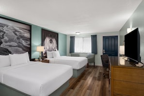 Habitación de hotel con dos camas, un escritorio, una silla, un televisor y un amplio ventanal con cortinas.