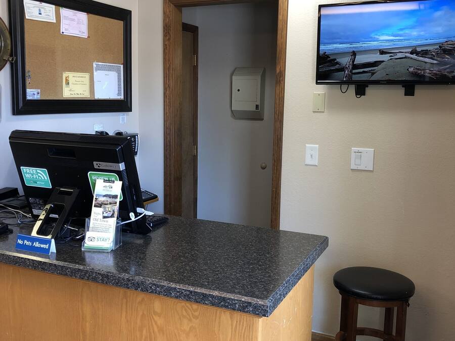 A reception desk with a computer, a sign prohibiting pets, and a television displaying a beach scene.