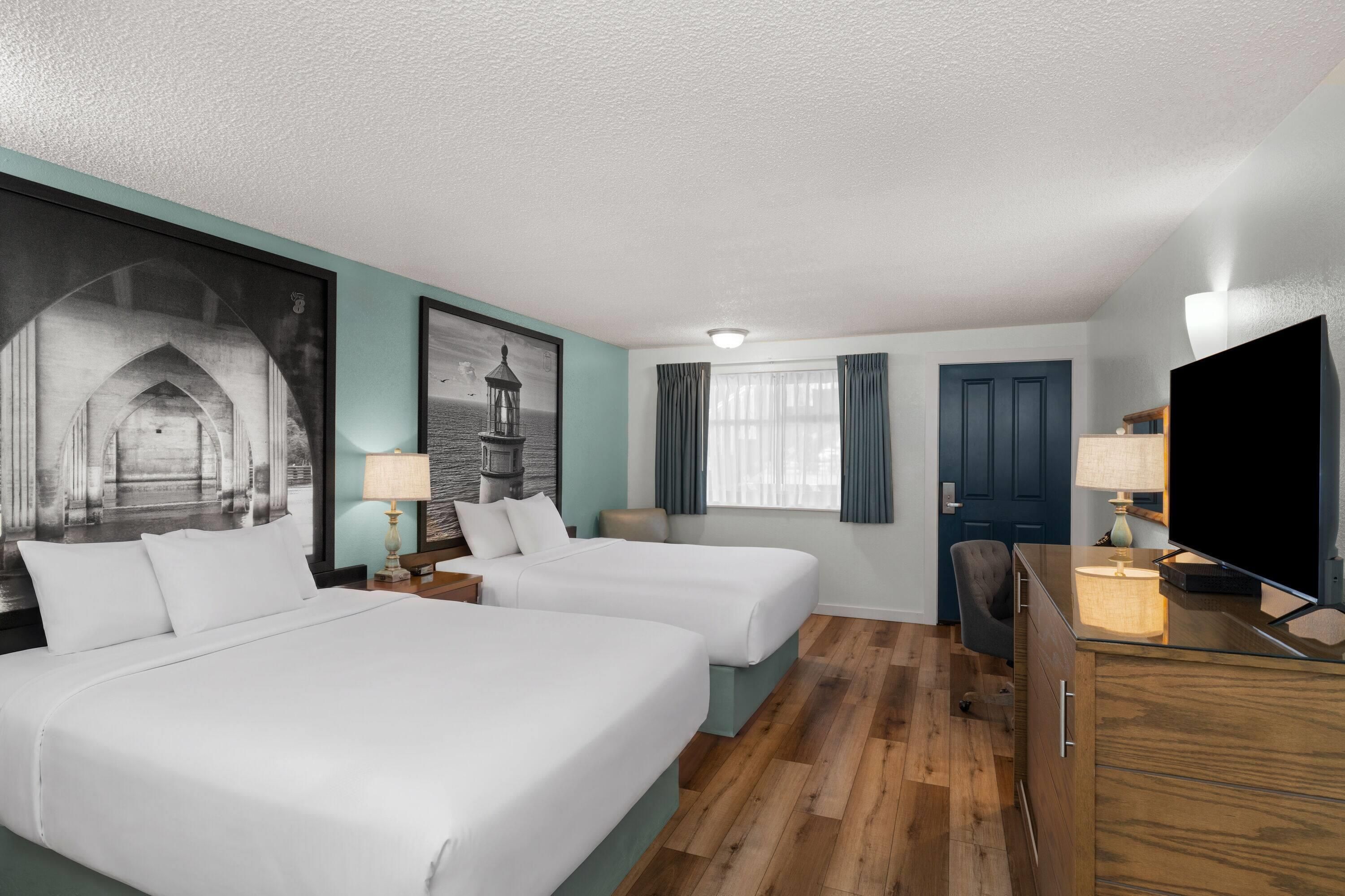 A hotel room with two beds, a desk, a television, and a large framed picture on the wall.