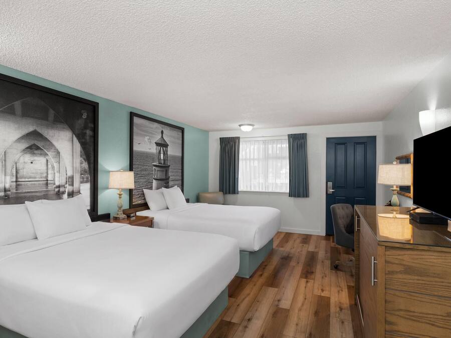 A hotel room with two beds, a desk, a television, and a large framed picture on the wall.