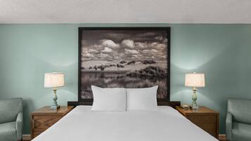 A hotel room with a large bed, two nightstands, two lamps, and a wall-mounted picture of a landscape.
