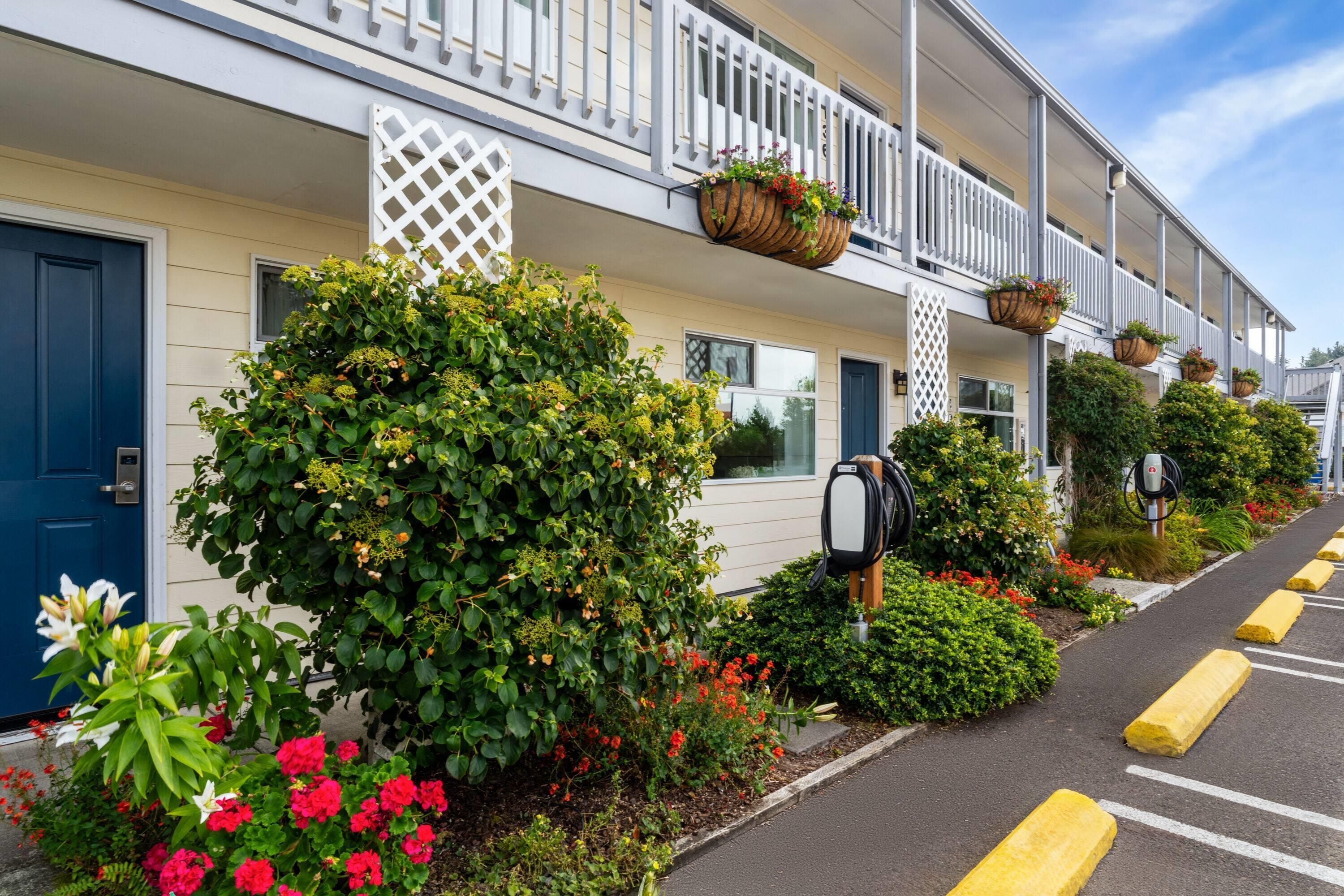 A row of hotel rooms with white railings, a mailbox, and a parking area with yellow bollards.