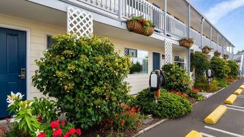 A row of hotel rooms with white railings, a mailbox, and a parking area with yellow bollards.