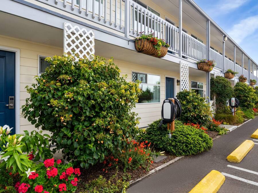 Fila de habitaciones de hotel con barandillas blancas, un buzón y un área de estacionamiento con bolardos amarillos.