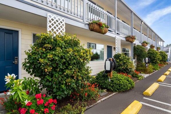 A row of hotel rooms with white railings, a mailbox, and a parking area with yellow bollards.