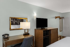 Habitación de hotel con cama, escritorio con lámpara, televisor, mueble de madera y luz en la pared.