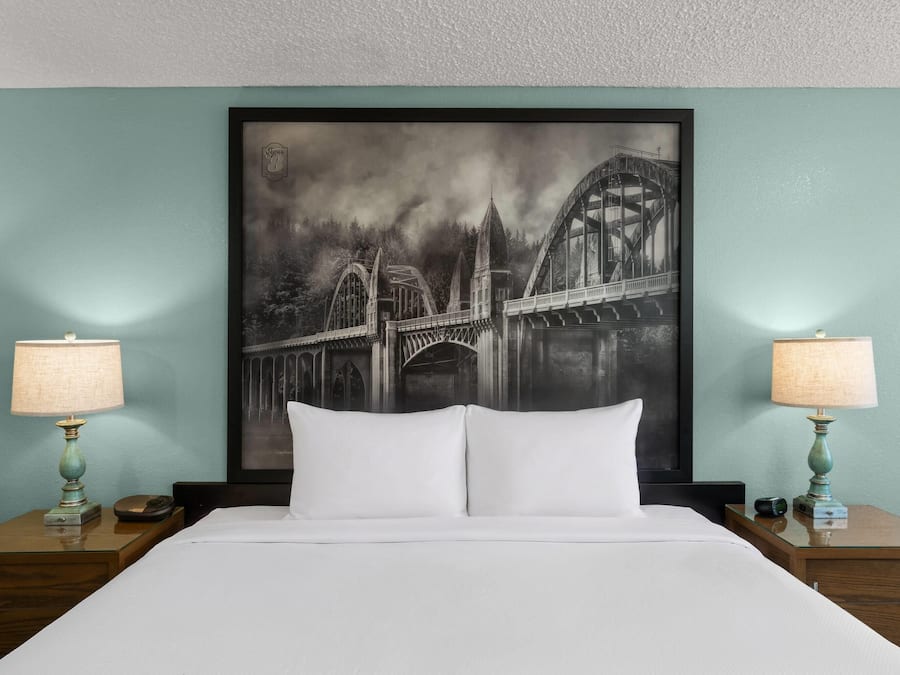 Habitación de hotel con una cama grande, dos lámparas de noche y un cuadro de un puente en la pared.