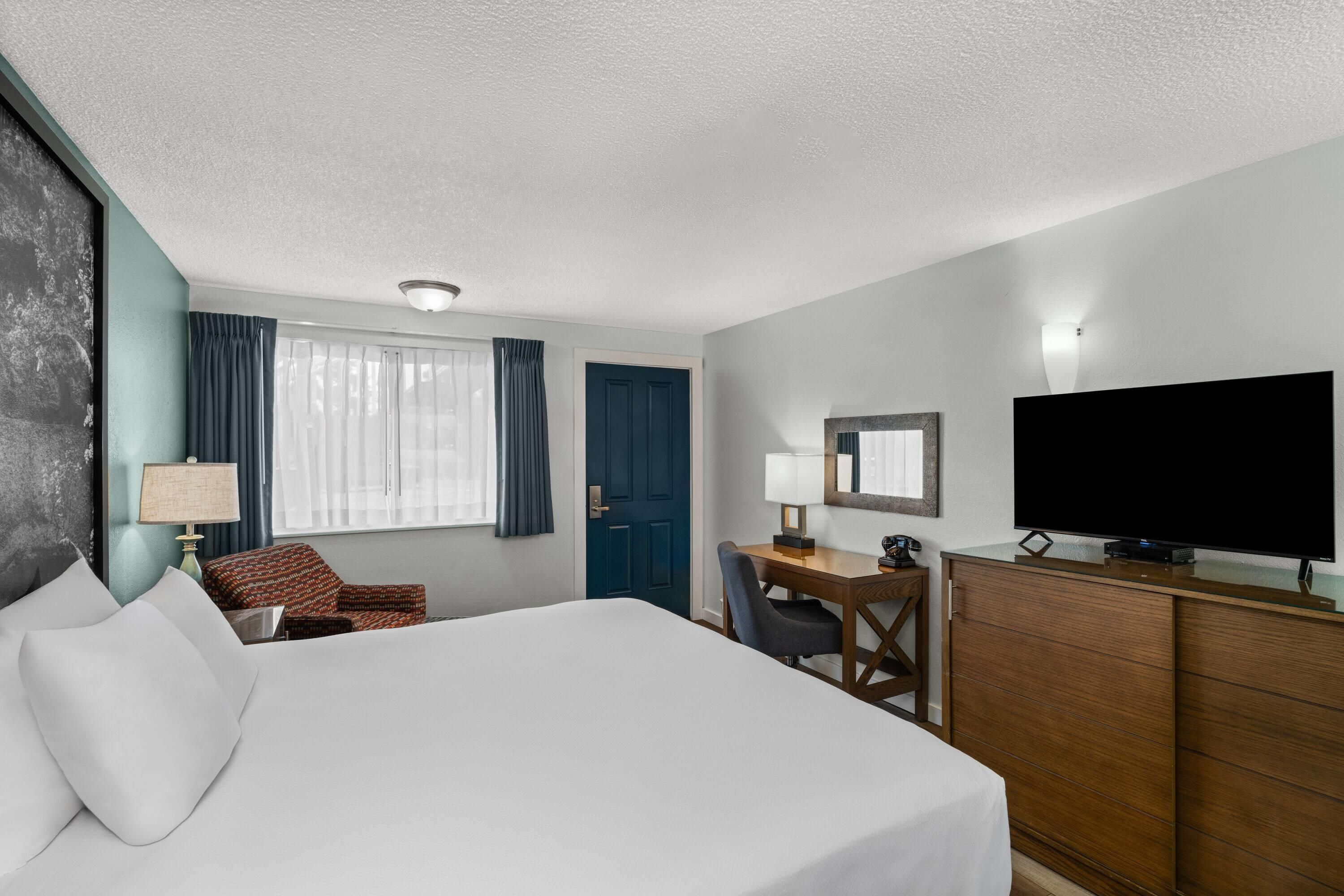 A hotel room with a bed, a desk, a chair, a television, and a dresser.