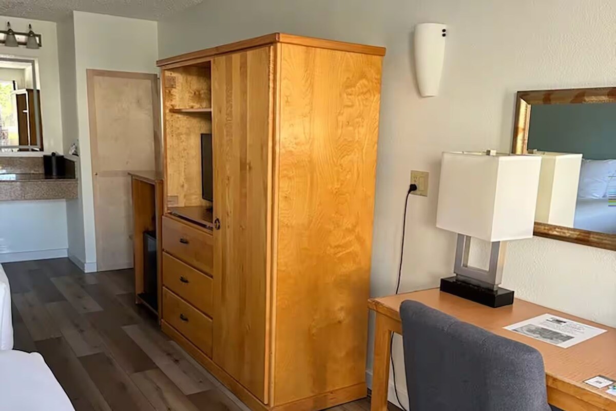 Habitación de hotel con un armario de madera, un escritorio con lámpara, un espejo y vistas al exterior.
