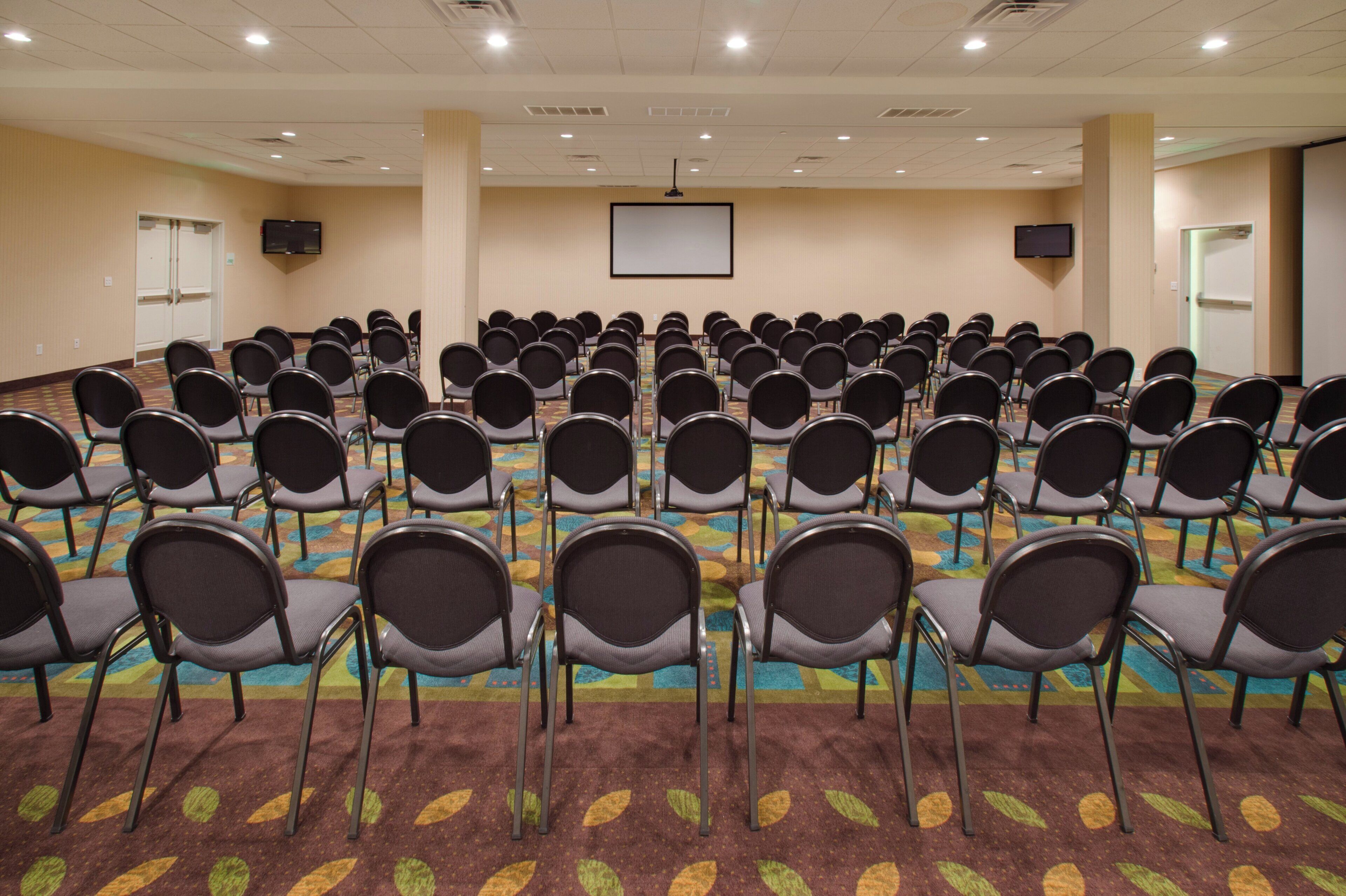 A conference room with rows of chairs, a projector screen, and a carpeted floor.