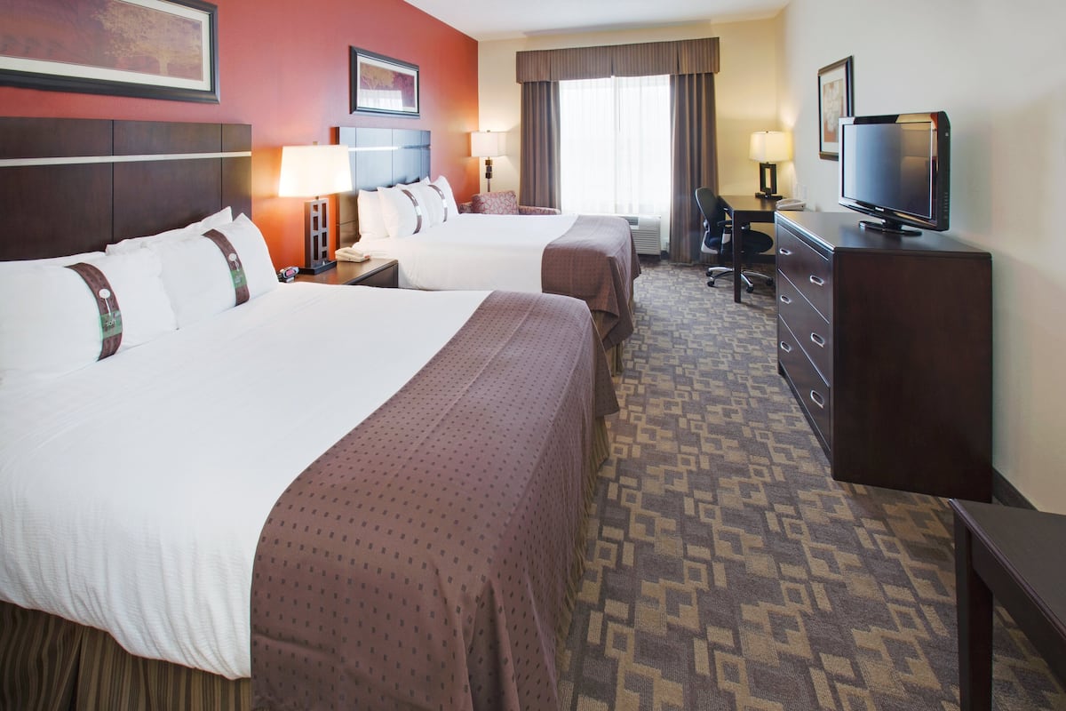 A hotel room with two beds, a desk, a television, and a chair.