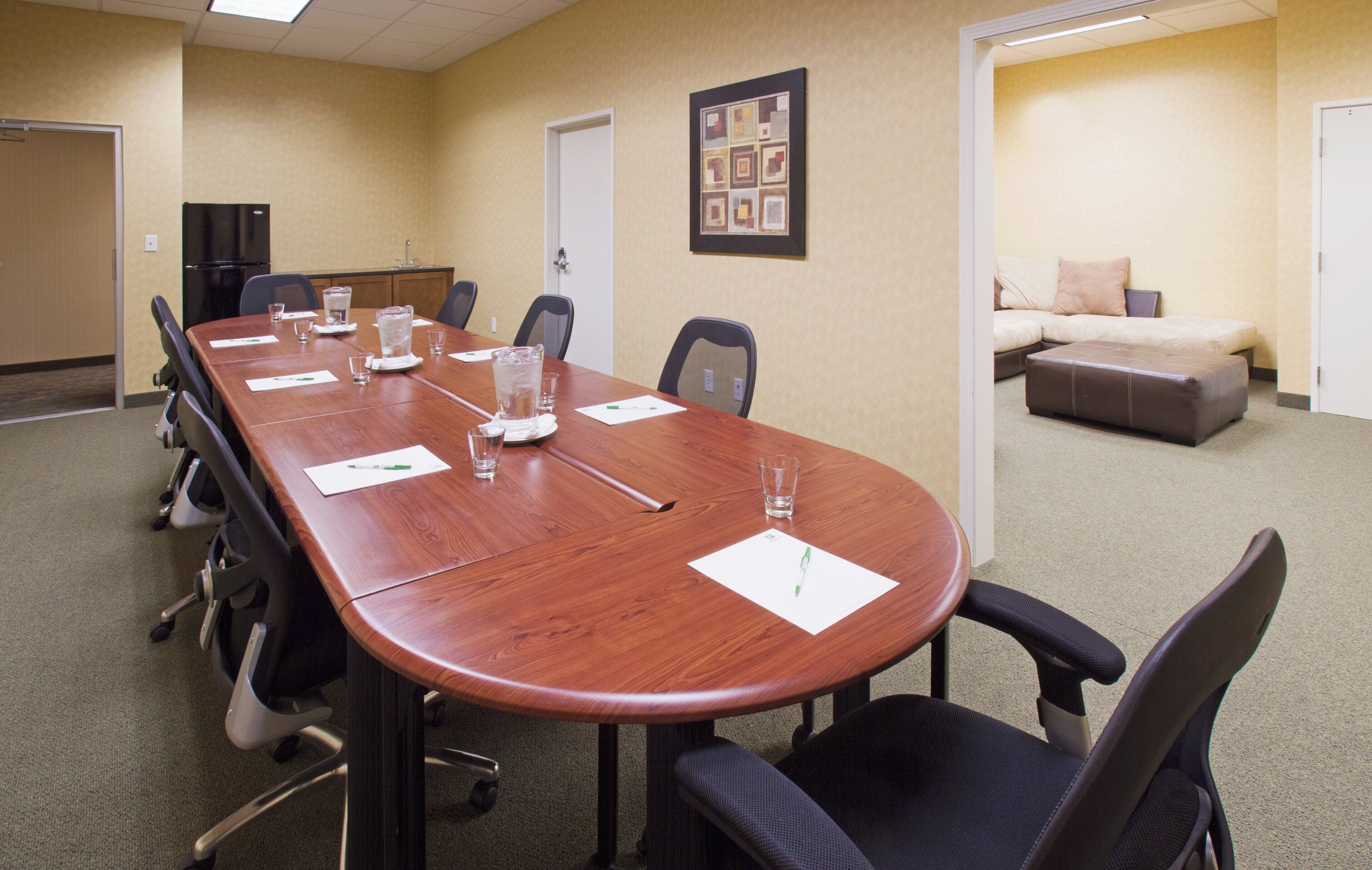 A conference room with a long table, chairs, and a sofa in the background.