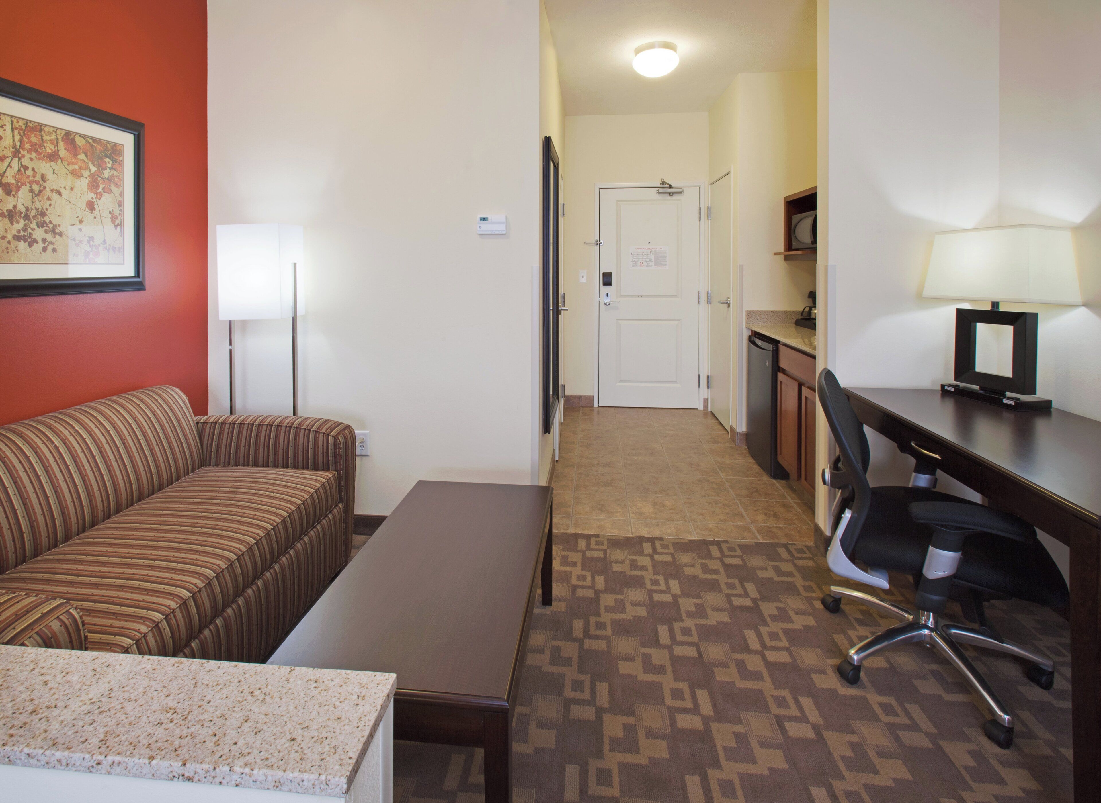 A hotel room with a striped sofa, a small table, a desk with a chair, a lamp, and a television.