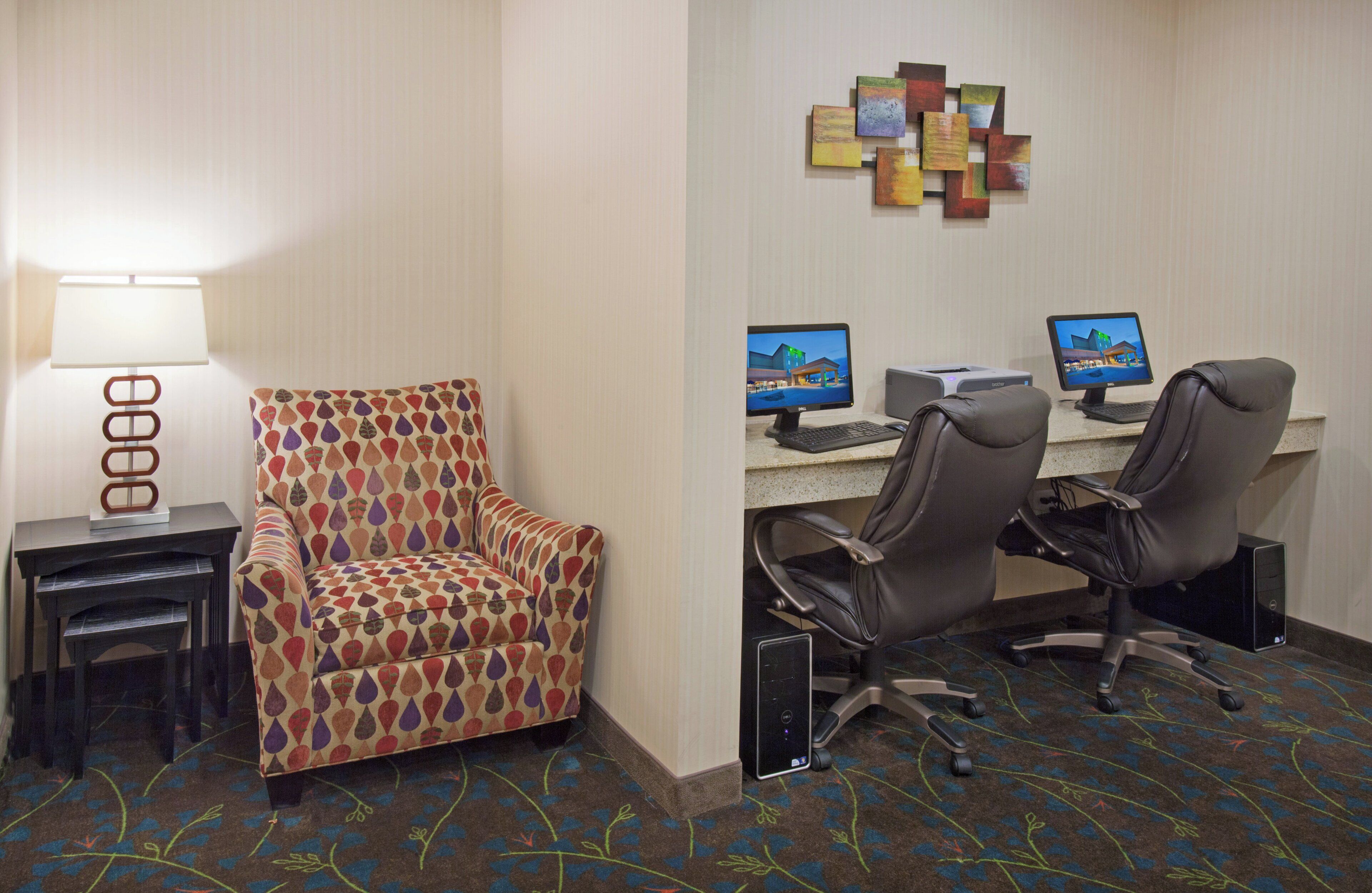 Una habitación de hotel con un sillón estampado, dos escritorios con computadoras, una lámpara y una alfombra con diseño floral.