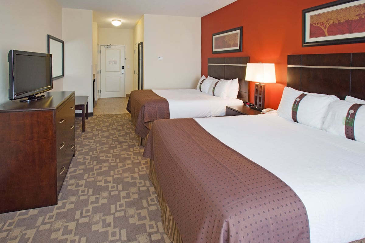 A hotel room with two beds, a TV, a desk, and a lamp.