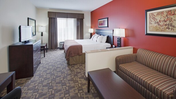 A hotel room with a bed, a sofa, a desk, a television, and a window with curtains. - Holiday Inn Lincoln Southwest by IHG (Lincoln)
