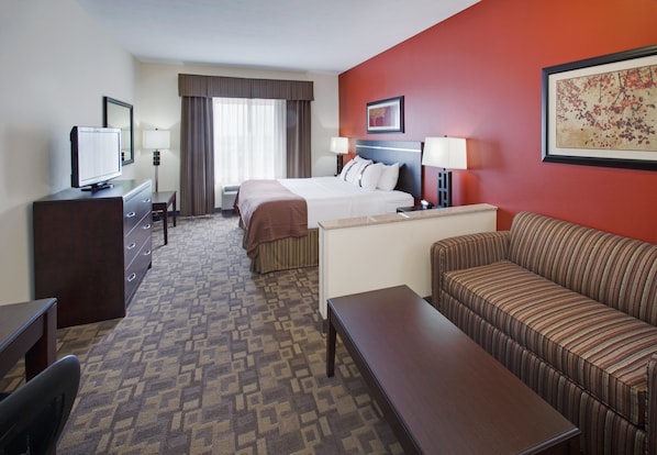 A hotel room with a bed, a sofa, a desk, a television, and a window with curtains.