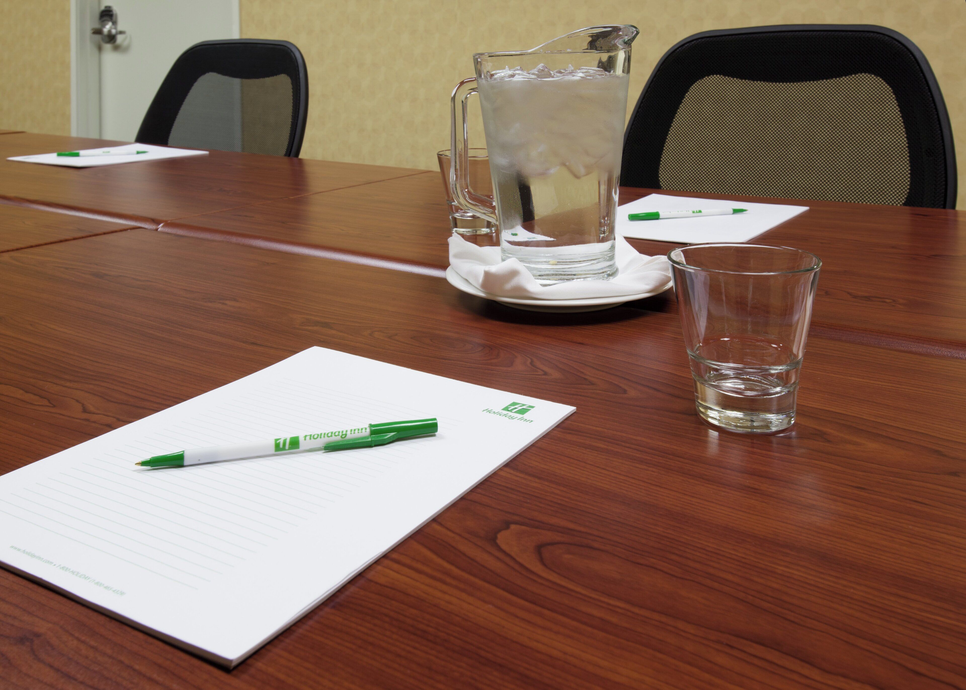 A conference table with a notepad, pen, glass of water, and a pitcher of water.
