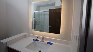 A bathroom with a white sink, a mirror above it, and a glass shower door. - Holiday Inn Lincoln Southwest by IHG (Lincoln)