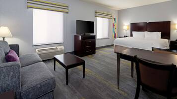 Quarto de hotel com cama, televisão, escrivaninha e área de estar.