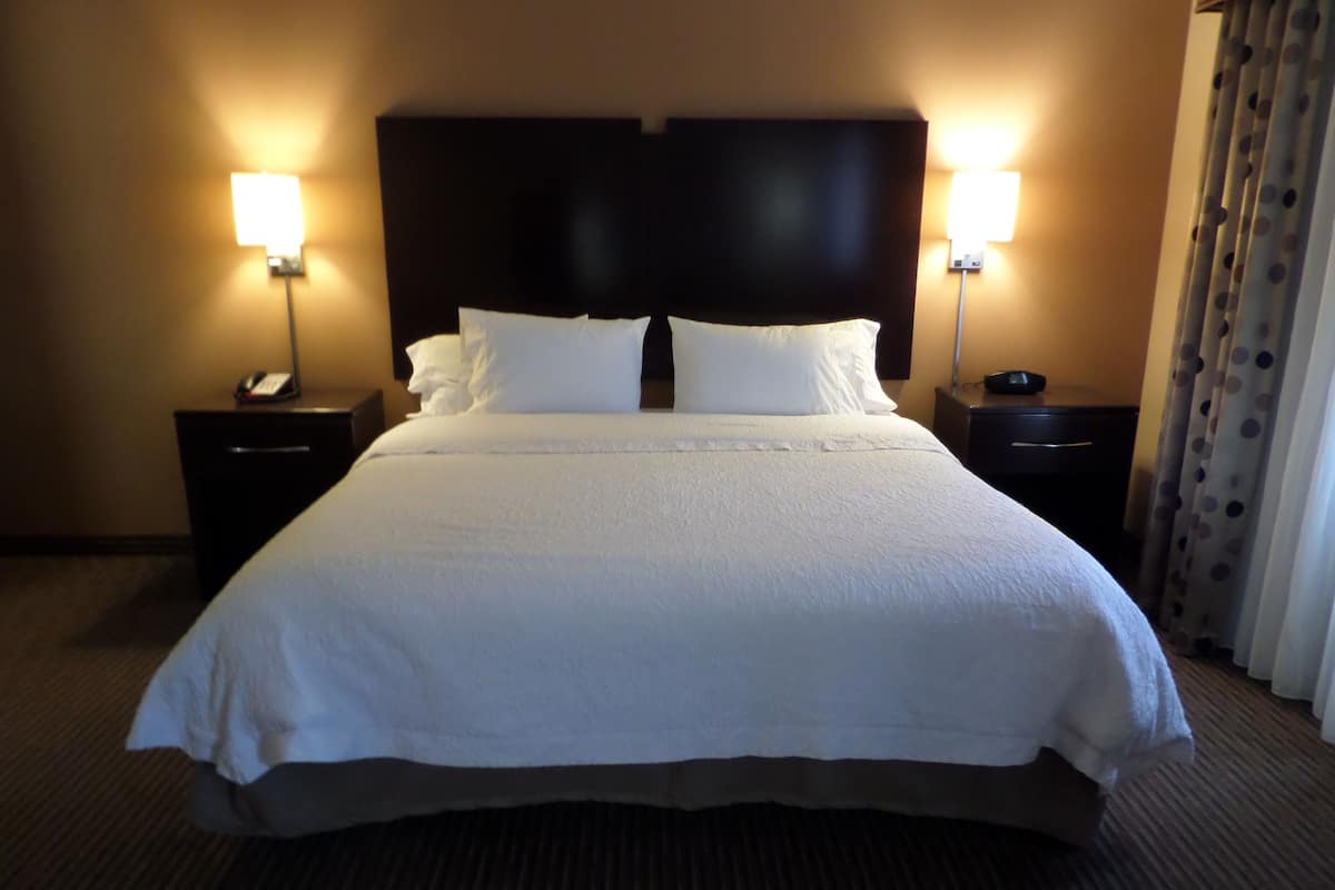 A large bed with a dark headboard, two bedside tables with lamps, and a curtain on the right.