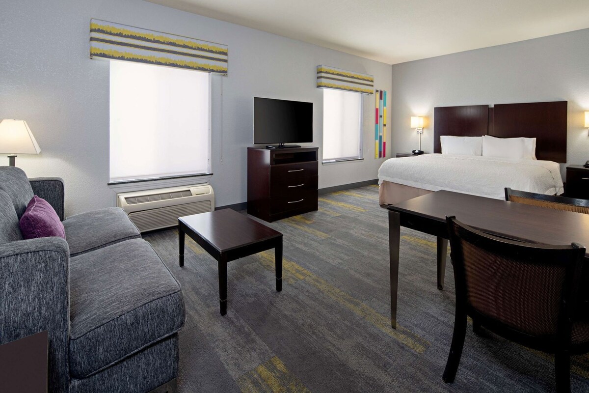 A hotel room with a bed, a desk, a chair, a TV, and a dresser.