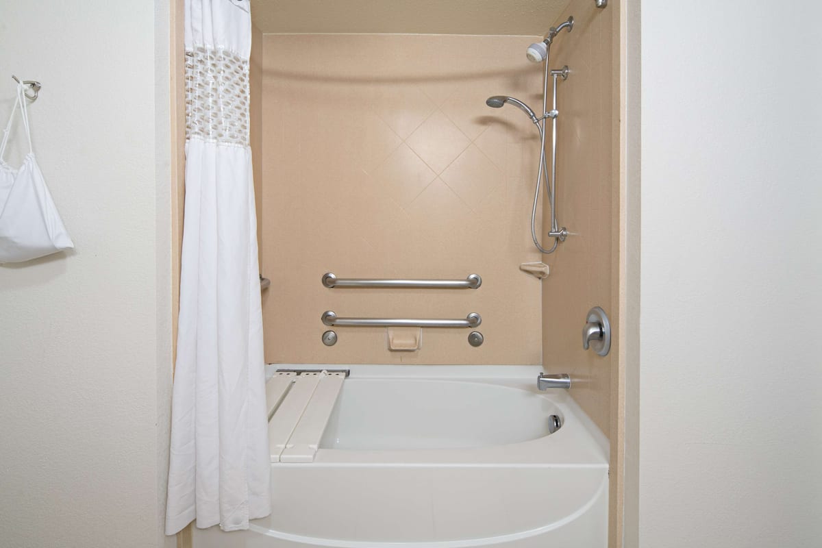 A bathroom with a white bathtub, grab bars, a showerhead, and a towel rack.