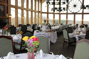 Un restaurant doté de nombreuses tables dressées pour le service, de grandes fenêtres et d’un décor intérieur rustique.