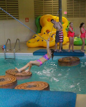 Une piscine avec des pierres plates en bois pour traverser, une balançoire à corde et des structures gonflables pour jouer.