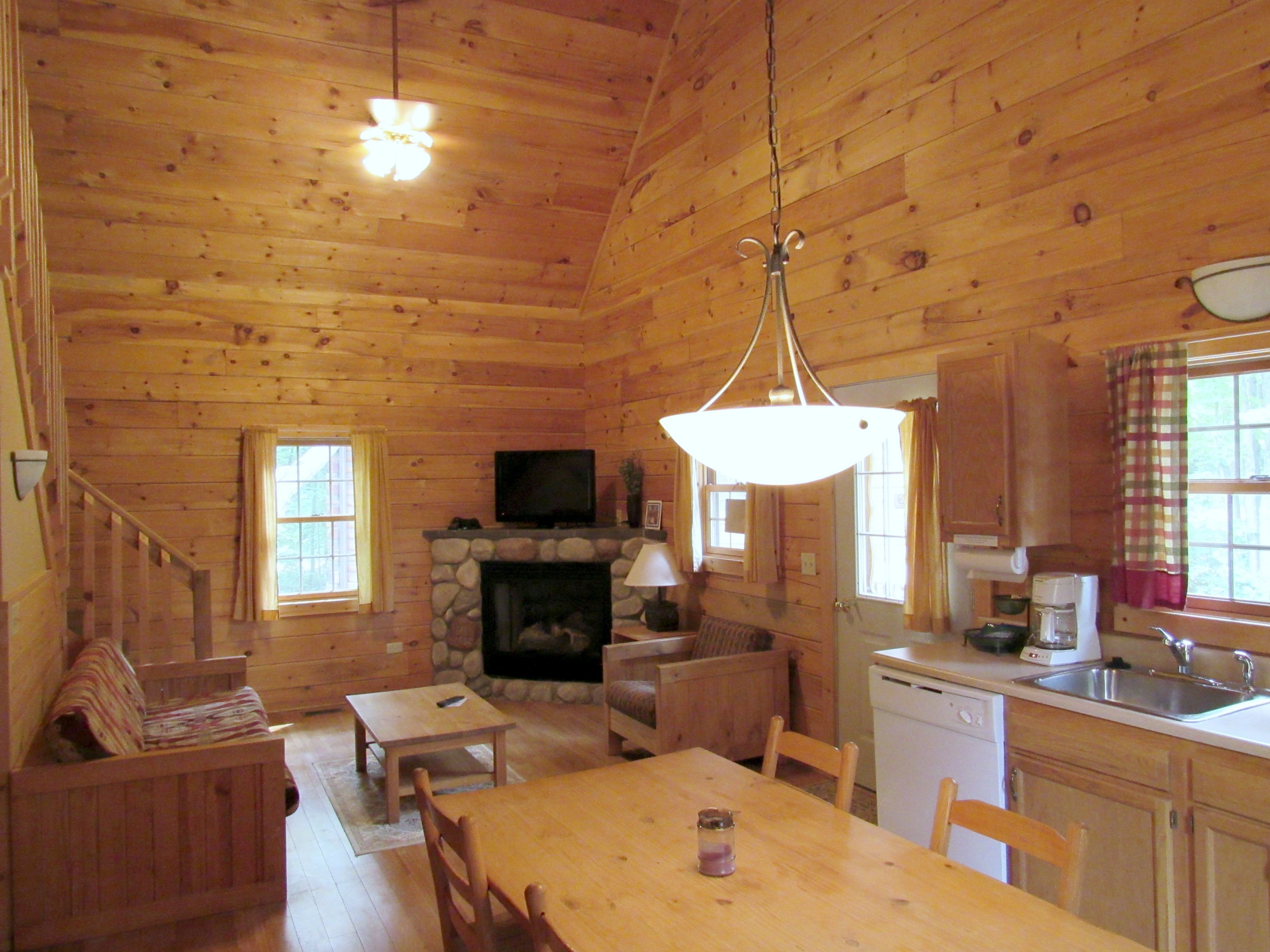 L’intérieur d’une cabane en rondins, avec une cheminée en pierre, des meubles en bois, un téléviseur et un coin cuisine.