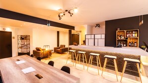 Un espace bar moderne avec un comptoir en bois, des tabourets de bar et un coin salon comprenant un canapé et des fauteuils.