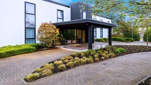 Un bâtiment moderne doté d’une entrée abritée, de chemins pavés et de jardins aménagés.