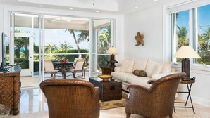 A spacious living area with wicker furniture, a ceiling fan, and a view of palm trees through large windows. - Grandview on Grace Bay (Providenciales)