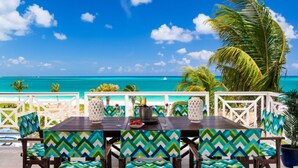 A dining area with a view of the ocean, featuring a table with chairs and a white railing. - Grandview on Grace Bay (Providenciales)