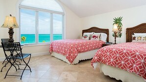 A bedroom with two beds, a window with a view of the ocean, a chair, and a lamp. - Grandview on Grace Bay (Providenciales)