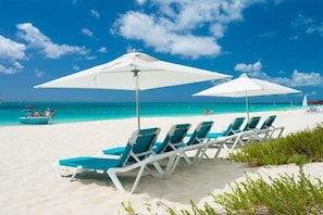 A beach with white umbrellas and blue lounge chairs. - Grandview on Grace Bay (Providenciales)