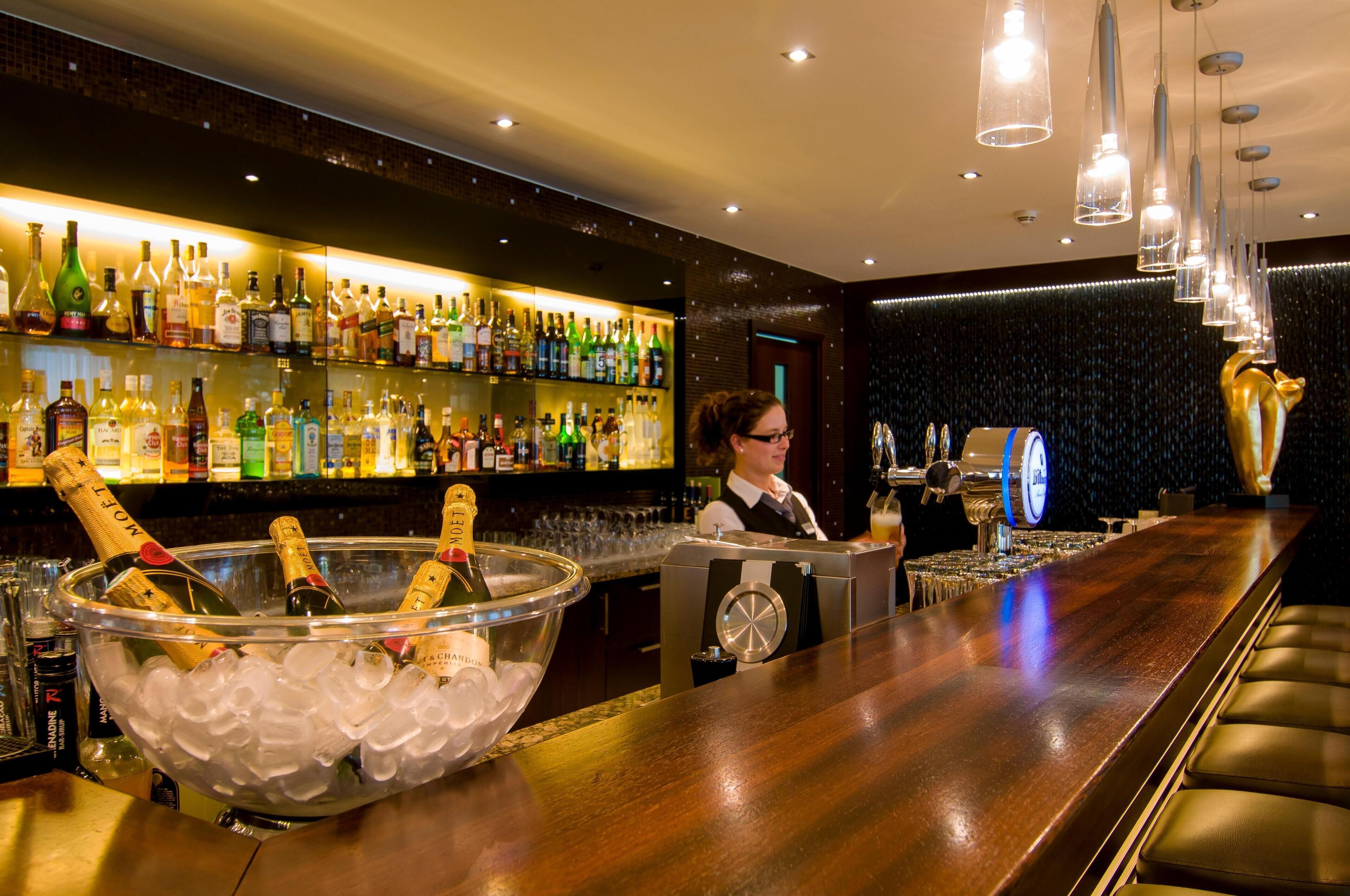 A bar area with a variety of liquor bottles, a large ice-filled bowl with champagne bottles, and a bartender at the counter.