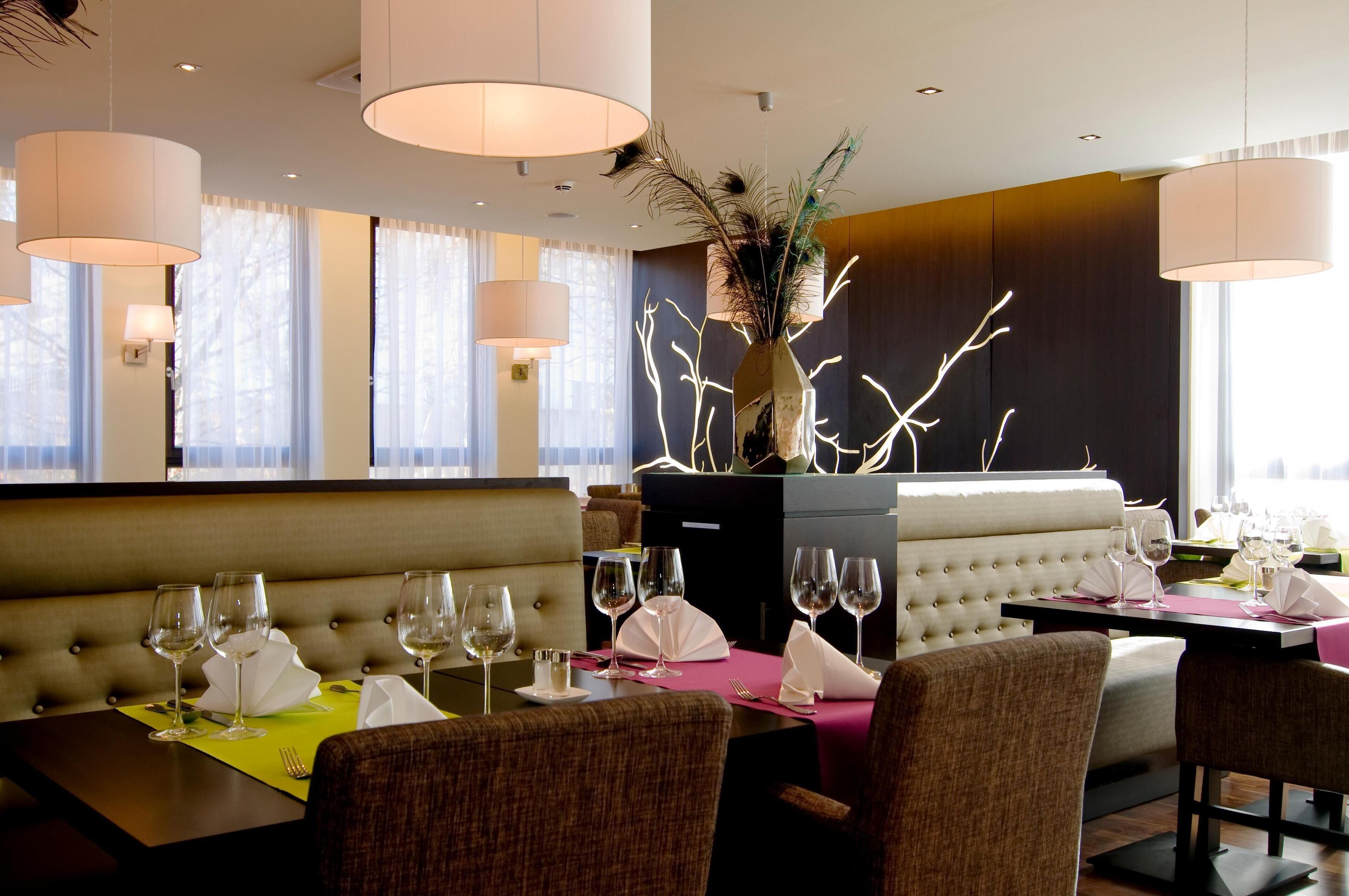 Ein Restaurant mit einer erhöhten Sitzbank, einer Vase mit Zweigen und mehreren Weingläsern auf den Tischen.