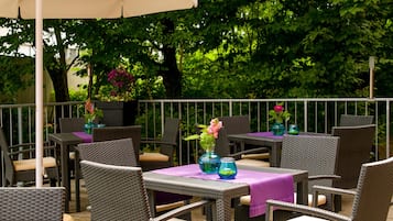 Ein Außenbereich mit Terrassenmöbeln aus Rattan, Tischen mit lila Tischdecken und Vasen mit Blumen.