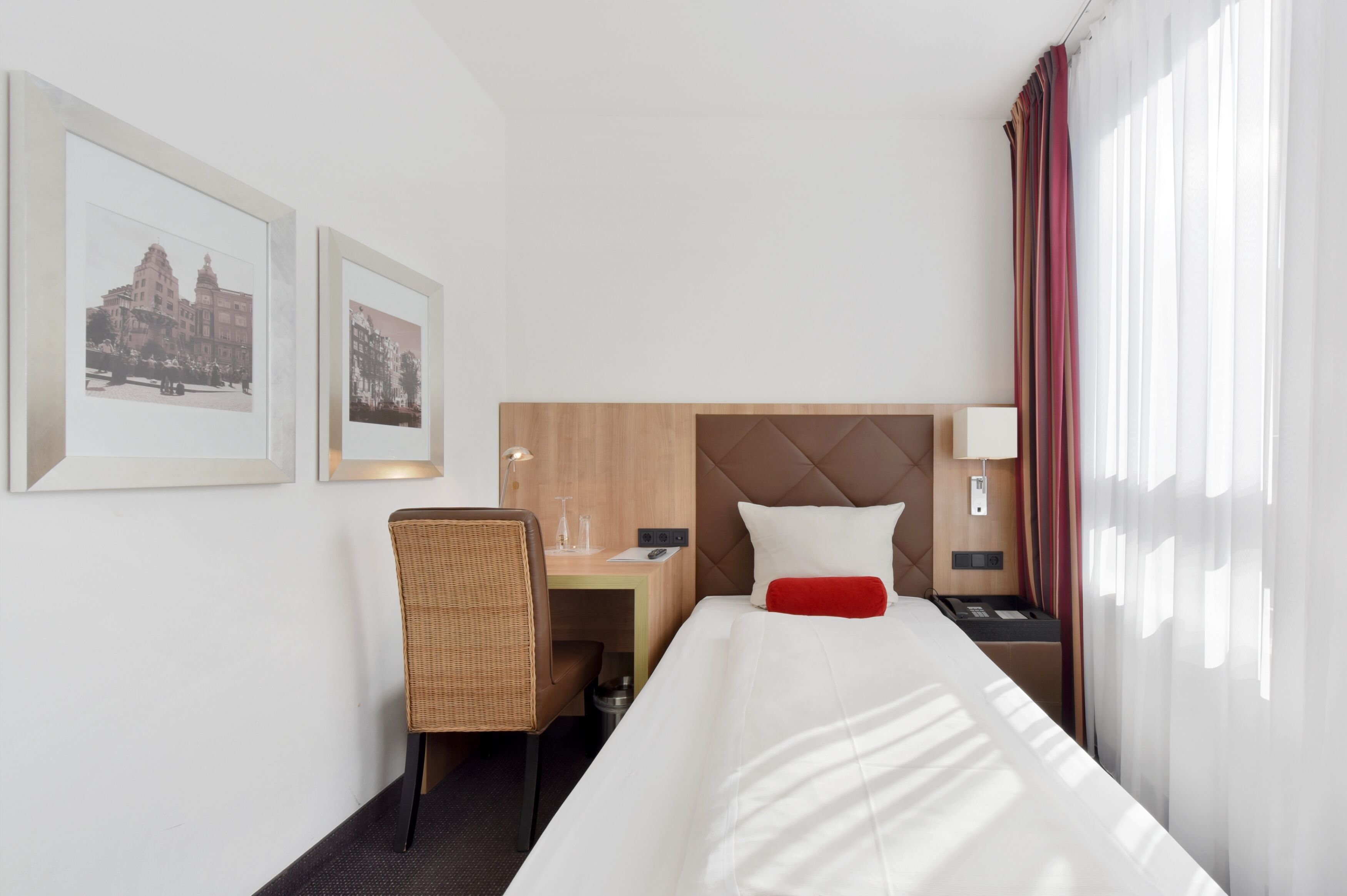 Habitación de hotel con cama, escritorio, silla, mesita de noche y dos cuadros en la pared.