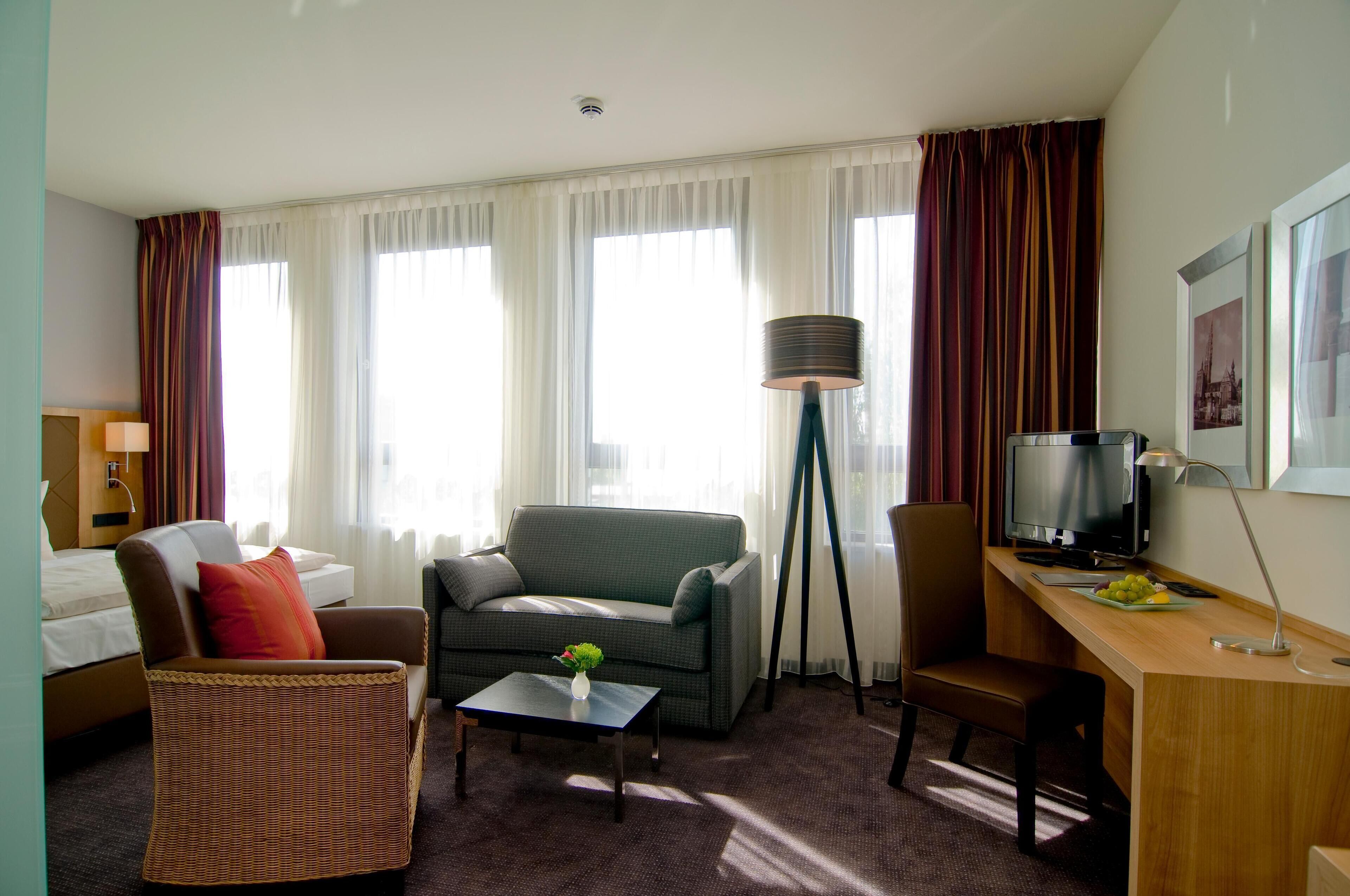 Hotellihuone, jossa on sänky, sohva, tuoli, työpöytä, televisio ja lamppu.