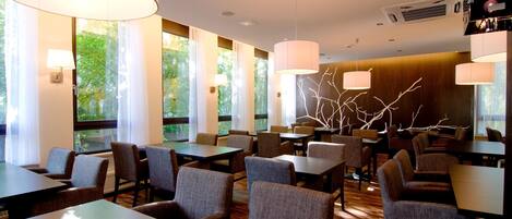 Un restaurante moderno con mesas y sillas de madera, ventanas amplias e iluminación colgante.