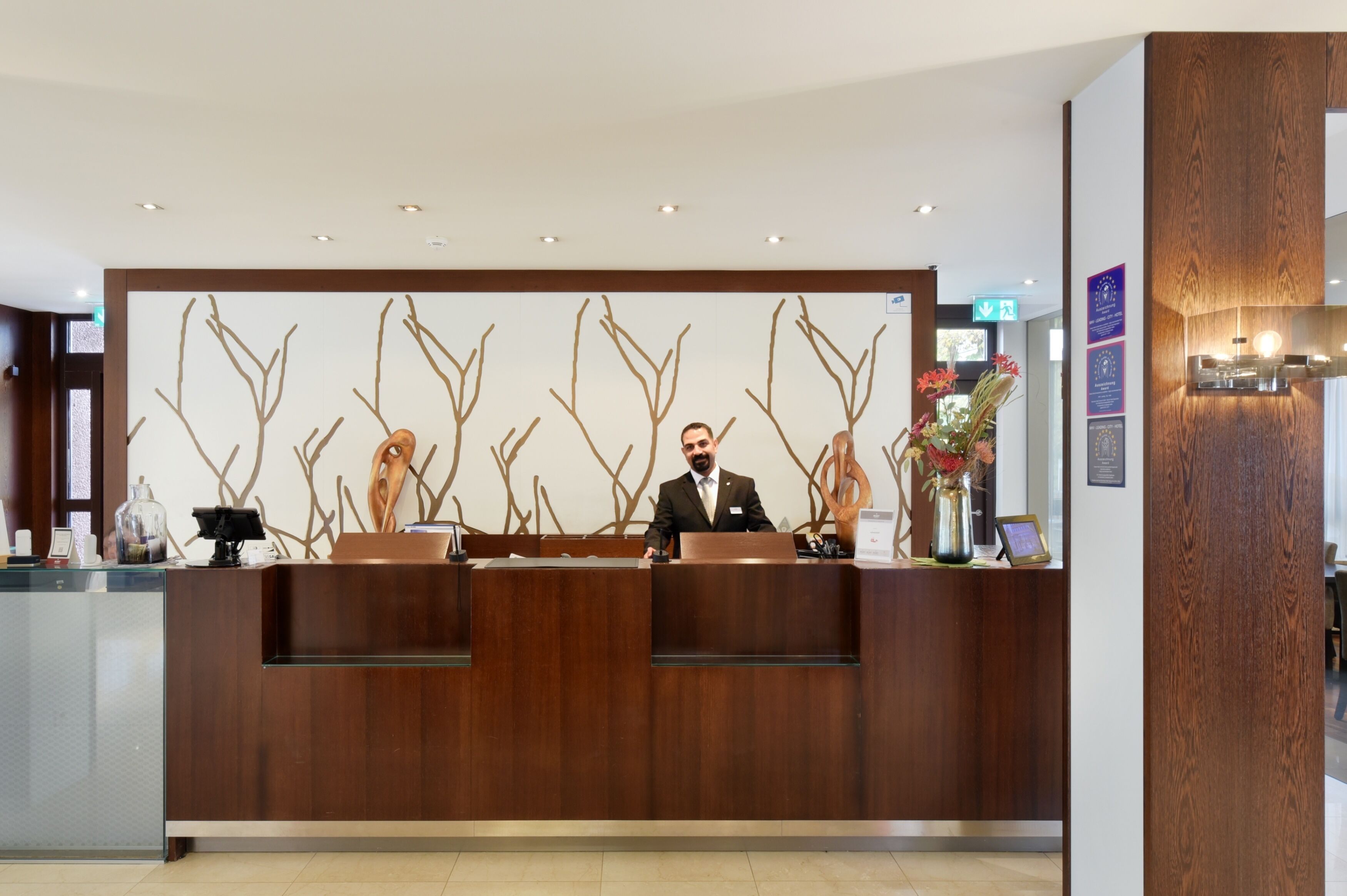 A reception desk with a modern design, featuring a wooden finish and a decorative wall with abstract branches.