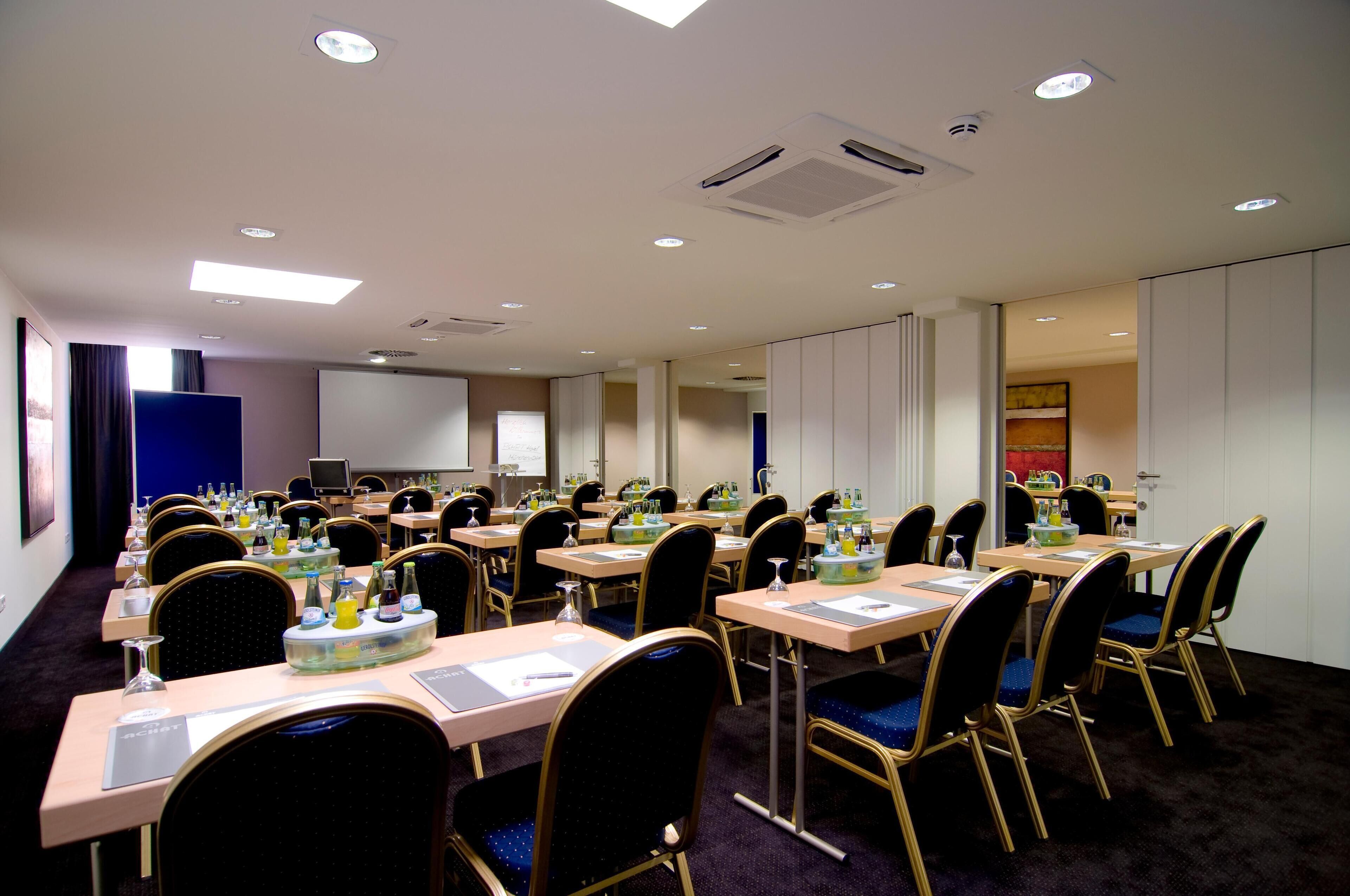 A conference room with multiple tables and chairs, equipped with water bottles, glasses, and notepads.